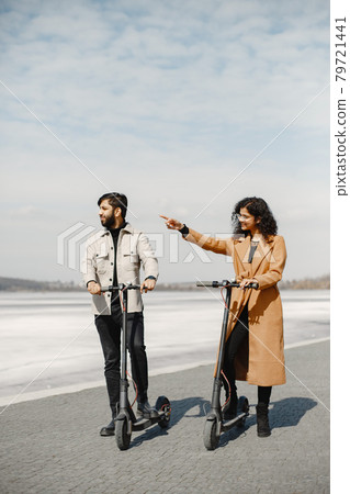Interracial young couple with scooters in the city background Interracial young couple with scooters in the city background 79721441