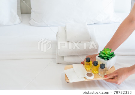 Hands of hotel maid put a set of hotel amenities (such as towels, shampoo, soap etc) on the bed. Hotel amenities is something of a premium nature provided in addition to the room when renting a room. Hands of hotel maid put a set of hotel amenities (such as towels, shampoo, soap etc) on the bed. Hotel amenities is something of a premium nature provided in addition to the room when renting a room. 79722353