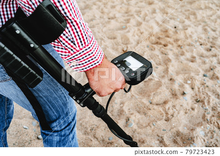 Male hand holding metal detector device above the ground 79723423