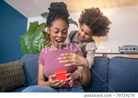 Enthusiastic african american woman and lovely daughter with gift. Enthusiastic african american woman and lovely daughter with gift. 79724276