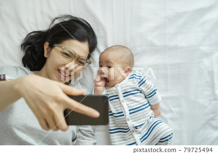 mother and newborn baby lying on bed having fun taking selfie photo mother and newborn baby lying on bed having fun taking selfie photo 79725494