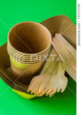 Wooden forks and paper cups with plates on green background. Eco friendly disposable tableware. Used in fast food, restaurants, takeaways, picnics. No plastic 79725709