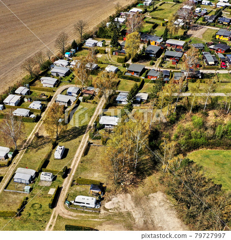 Aerial view of the edge of a campsite with a few cottages, caravans and tents on grassland Aerial view of the edge of a campsite with a few cottages, caravans and tents on grassland 79727997