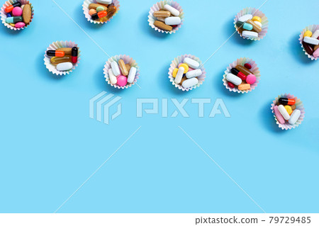Colorful tablets with capsules and pills in cupcake wrappers on blue background. Colorful tablets with capsules and pills in cupcake wrappers on blue background. 79729485