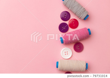 Multicolored thread spools and buttons on pink background Multicolored thread spools and buttons on pink background 79731014