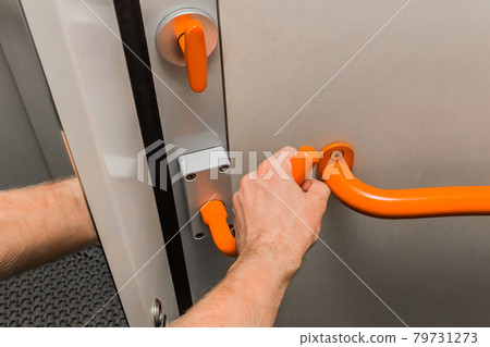 A man's hand holds on to a metal handle next to a handrail and opens a door in a modern electric train A man's hand holds on to a metal handle next to a handrail and opens a door in a modern electric train 79731273