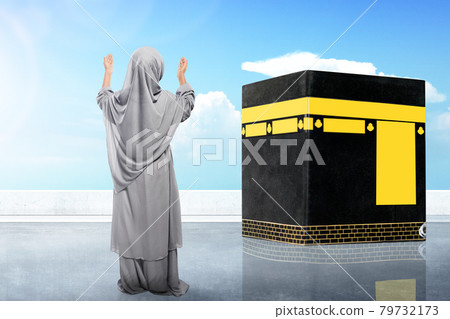 Rear view of Asian Muslim little girl in a veil standing and raised hands praying in front of the Kaaba Rear view of Asian Muslim little girl in a veil standing and raised hands praying in front of the Kaaba 79732173