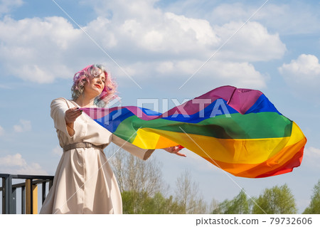 Caucasian woman with curly colored hair holding lgbt flag. Lesbian woman holding a rainbow flag outdoors 79732606