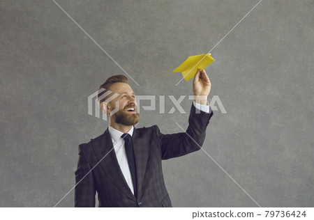 Happy young business executive flying paper plane standing isolated on grey background Happy young business executive flying paper plane standing isolated on grey background 79736424