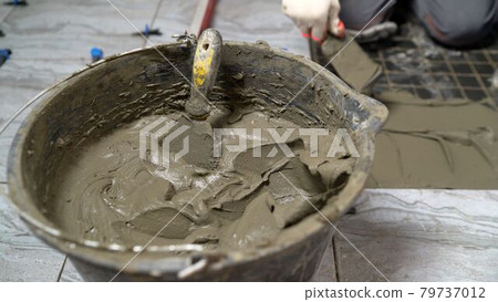A device for mixing ceramic tile adhesive. Glue bucket. Mixing glue in a bucket. A worker mixes tile adhesive in a bucket. A device for mixing ceramic tile adhesive. Glue bucket. Mixing glue in a bucket. A worker mixes tile adhesive in a bucket. 79737012