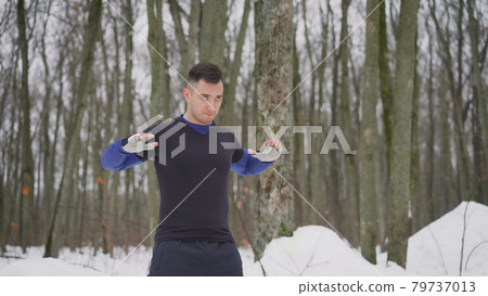 Outdoor seasonal sports. Full length portrait of positive mature guy doing exercises before jogging at snowy winter park. The guy is doing exercises in the park in winter. Outdoor seasonal sports. Full length portrait of positive mature guy doing exercises before jogging at snowy winter park. The guy is doing exercises in the park in winter. 79737013