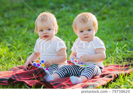 Two twin girls play with colored toys on a blanket on a sunny summer day 79738620