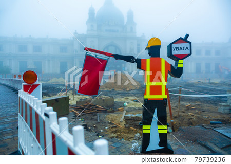 Road sign in the shape of a road worker, urging drivers to slow down on a section of road works 79739236