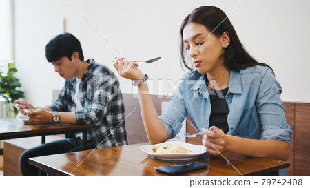 Young Asian man and woman having lunch meal in local restaurant, sit in social distance Young Asian man and woman having lunch meal in local restaurant, sit in social distance 79742408