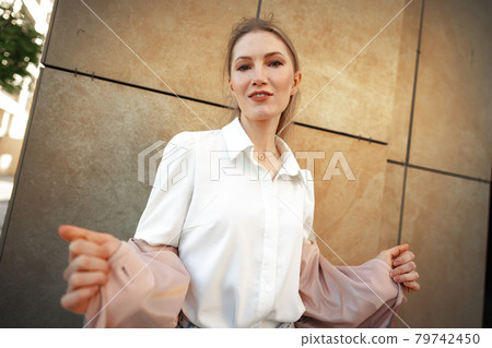 Stylish girl in jeans and white cotton blouse posing near gray wall Stylish girl in jeans and white cotton blouse posing near gray wall 79742450