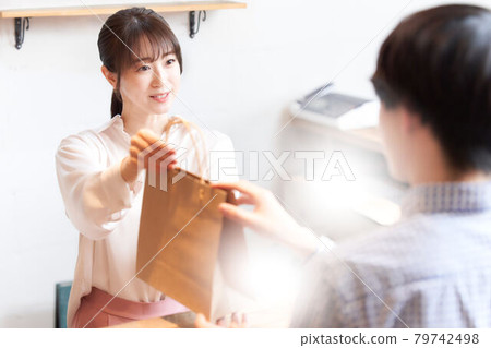 Female staff handing products in paper bags to customers Female staff handing products in paper bags to customers 79742498
