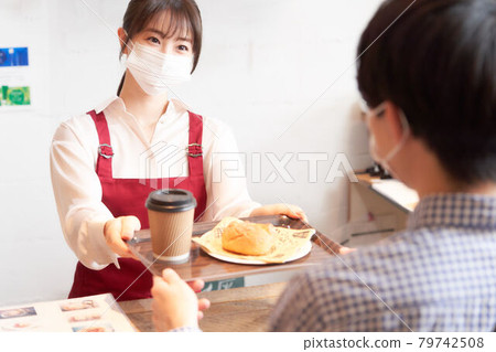 A female clerk wearing a mask handing an order to a customer at the counter 79742508