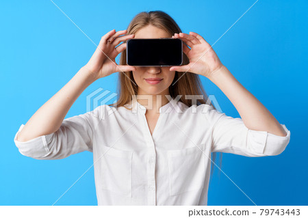 Beautiful young woman showing smartphone screen against blue background 79743443