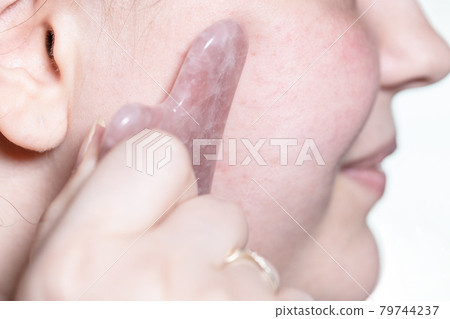 massaging female cheek with quartz scraper closeup 79744237