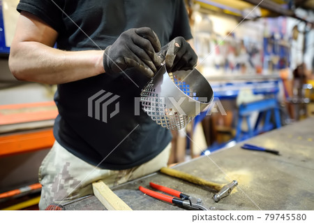 Metalwork craftsman making handmade lamp at workshop. Man worker screws up the parts of lampshade. Diy. Small local business. Metalwork craftsman making handmade lamp at workshop. Man worker screws up the parts of lampshade. Diy. Small local business. 79745580