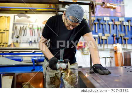 Metalwork craftsman cutting metal with grinder tools. Worker man in protection gloves and glasses working in the workshop. Small local business. Metalwork craftsman cutting metal with grinder tools. Worker man in protection gloves and glasses working in the workshop. Small local business. 79745581