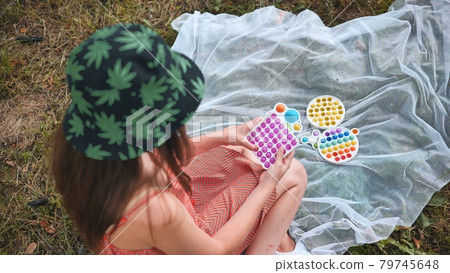 Teen girl plays with anti-stress popit and simple dimple toys in the park on a summer day. Teen girl plays with anti-stress popit and simple dimple toys in the park on a summer day. 79745648