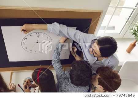 Female teacher explaing clock time to elementary student children in class 79745649