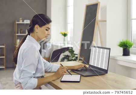 Woman sitting at office desk, working on laptop and tablet computers and using stylus pen Woman sitting at office desk, working on laptop and tablet computers and using stylus pen 79745652