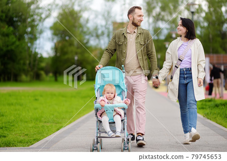Adorable toddler girl is riding into baby stroller during walk with her young loving parents . Active leisure for family with little kids. Happy childhood. 79745653