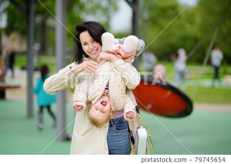 Toddler girl having fun on outdoor playground. Merry young mother swinging her little daughter. Spring/summer/autumn active leisure for family with kids. Toddler girl having fun on outdoor playground. Merry young mother swinging her little daughter. Spring/summer/autumn active leisure for family with kids. 79745654