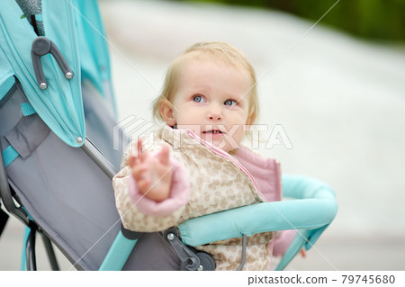 Adorable toddler girl is riding into baby stroller during stroll. Active leisure for family with little kids. Happy childhood. Adorable toddler girl is riding into baby stroller during stroll. Active leisure for family with little kids. Happy childhood. 79745680