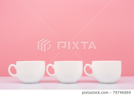 Three white ceramic cups in a row on white table against pink background 79746869