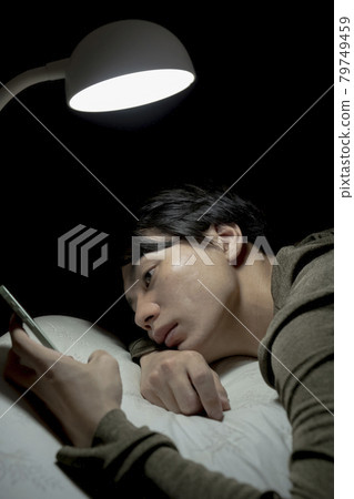 A man looking at a smartphone in bed in the middle of the night 79749459