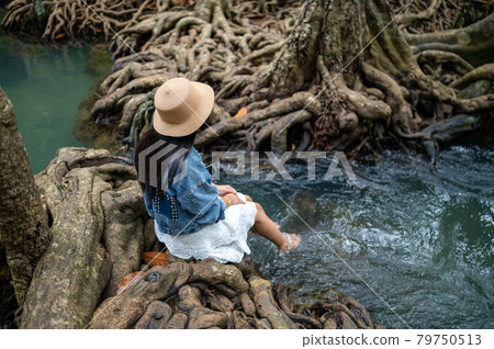 A woman swaying her feet in the water with the beautiful root of trees 79750513