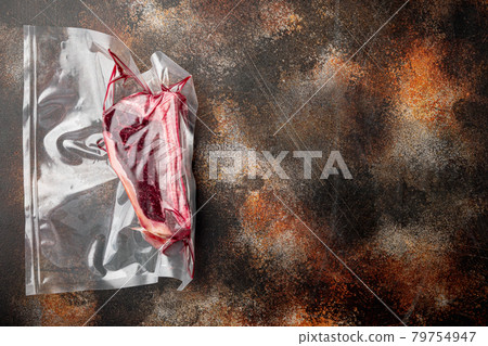 Raw beef meat Club or striploin on the bone steak in plastic airtight pack, on old dark rustic background, top view flat lay, with copy space for text 79754947