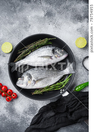 Pair of Seabream or dorado raw fish on grill pan with ingredients on grey white textured background, top view. 79754955