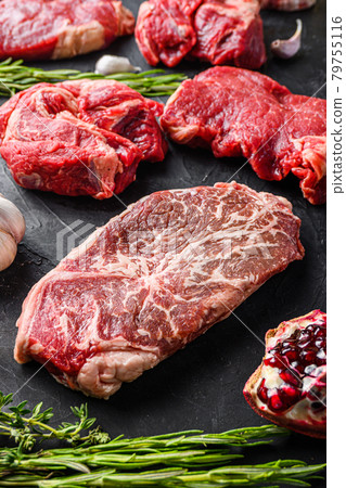Flat Iron beef steak cuts, with herbs, seasoning on black table, side view. 79755116