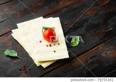 Dried uncooked lasagna pasta sheets, with seasoning and herb, on old dark wooden table background, with copy space for text 79755161