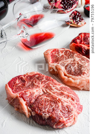 Beef cuts Chuck eye roll, top blade, rump steak with red wine in glass and bottle, herbs and pomegranate. Organic meat. White textured background. Side view vertical. Beef cuts Chuck eye roll, top blade, rump steak with red wine in glass and bottle, herbs and pomegranate. Organic meat. White textured background. Side view vertical. 79755196