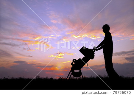 A young man pushing a stroller and taking a walk against the backdrop of the setting sun 79756070