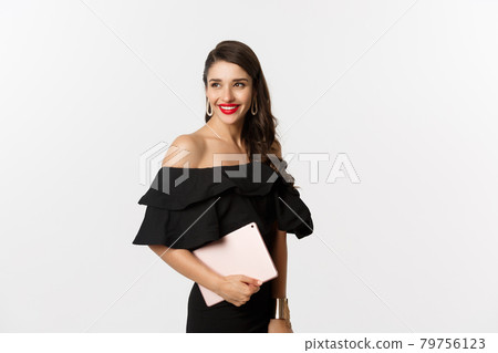 Fashion and shopping concept. Stylish young woman with glamour makeup, wearing black dress, holding digital tablet and smiling, white background 79756123