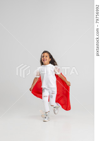 Small superhero. Little cute Caucasian girl in a red cape isolated over white studio background. Full length portrait Small superhero. Little cute Caucasian girl in a red cape isolated over white studio background. Full length portrait 79756992