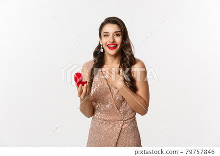 Image of beautiful woman in glamour dress receiving engagement ring, looking surprised and happy at camera, being proposed, standing over white background Image of beautiful woman in glamour dress receiving engagement ring, looking surprised and happy at camera, being proposed, standing over white background 79757846