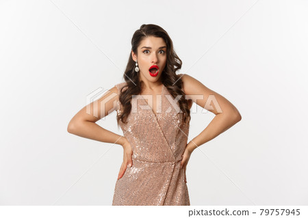 Image of attractive party woman in elegant dress, red lips, looking amazed and surprised, celebrating new year, standing over white background 79757945