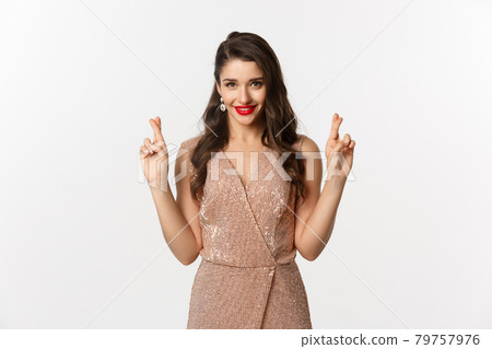 Concept of casino, celebration and party. Hopeful beautiful woman making a wish, cross fingers for good luck and looking confident, white background Concept of casino, celebration and party. Hopeful beautiful woman making a wish, cross fingers for good luck and looking confident, white background 79757976