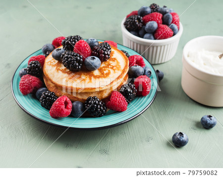 Stack of pancakes with raspberries and blueberries served in a dish on green background 79759082
