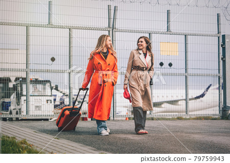 Two happy girls walking near airport, with luggage. Air travel, summer holiday Two happy girls walking near airport, with luggage. Air travel, summer holiday 79759943