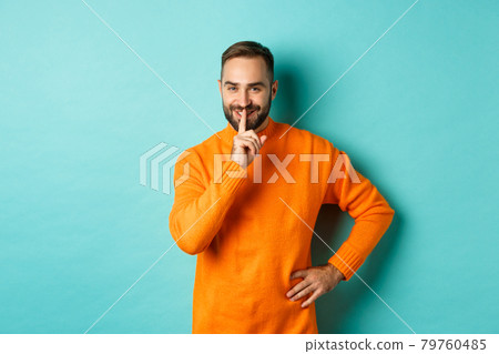 Happy man asking keep voice down, shushing and smiling, prepare surprise, hushing at camera, standing over turquoise background Happy man asking keep voice down, shushing and smiling, prepare surprise, hushing at camera, standing over turquoise background 79760485