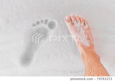 The men's leg stands next to its footprint on the beach sand close-up The men's leg stands next to its footprint on the beach sand close-up 79763253