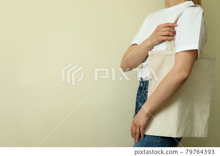 Young woman in blank t-shirt with bag against beige background Young woman in blank t-shirt with bag against beige background 79764393